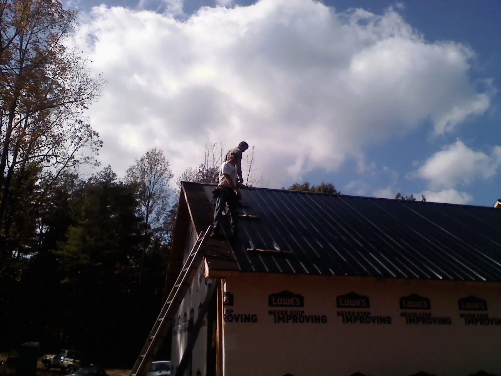 Roofer fastening dark metal panels high against a cloudy sky, from a Roof Inspection job in Boise