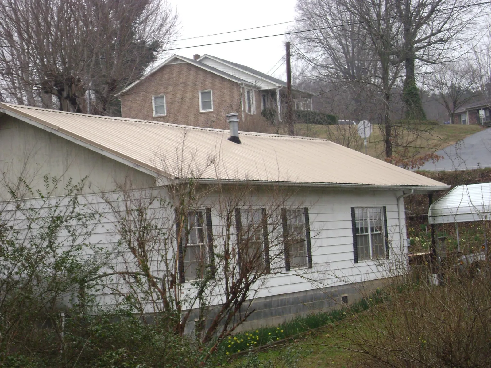 Tan metal roof on a white sided house set into a hillside — Commercial Roofing by Roofing Brothers in Boise